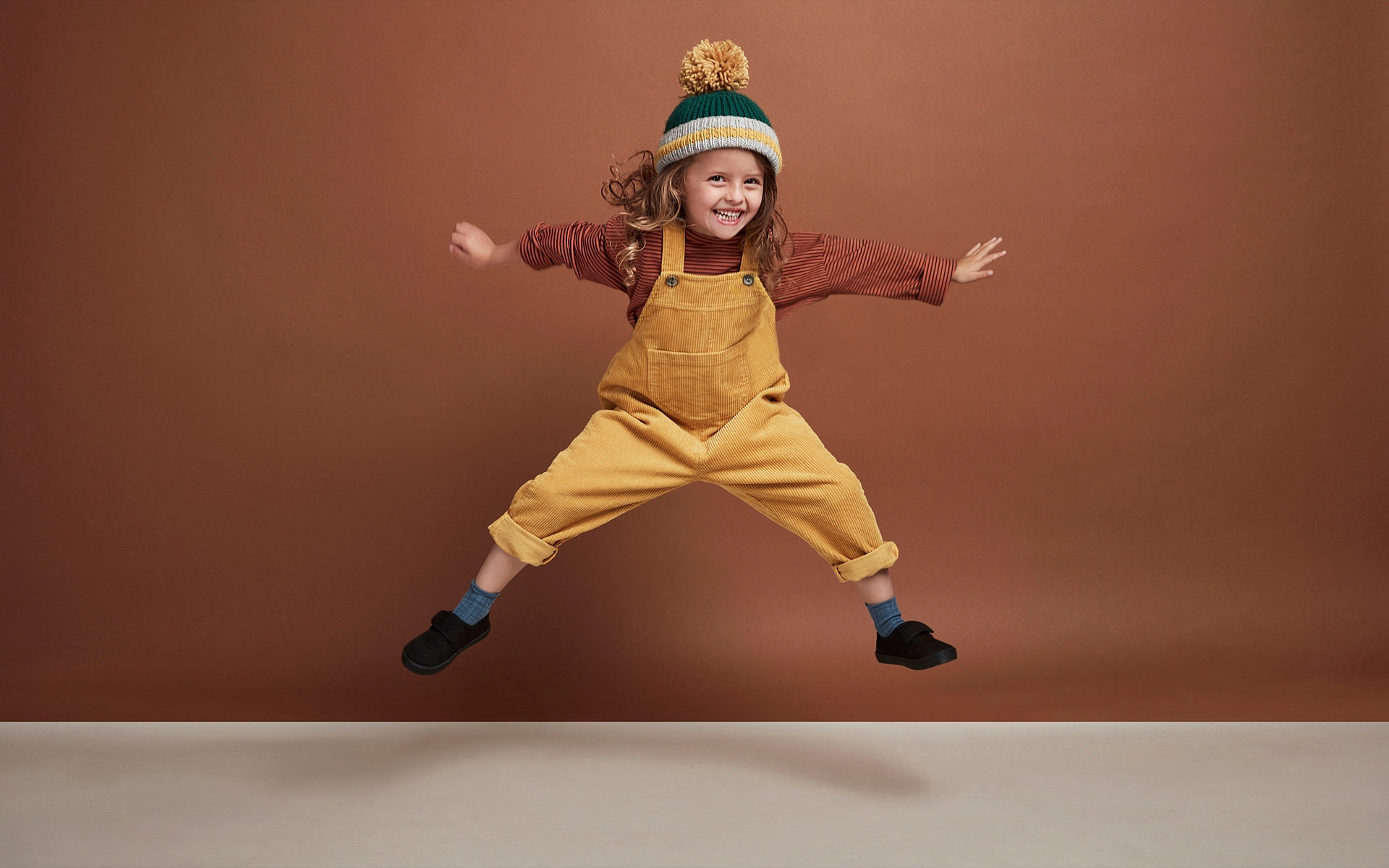 A child model jumping in the air on a clothing e commence photo shoot in front of a brown back drop in a photography studio
